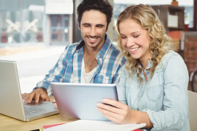 Two digital marketing colleagues collaborating on a strategy, reviewing analytics on a tablet and laptop.