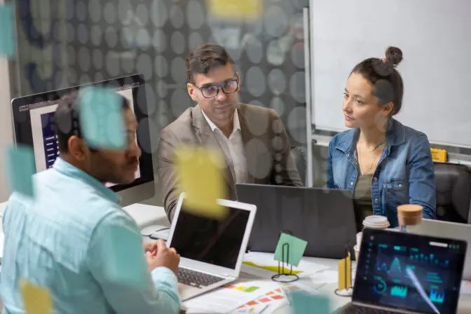 An SEO team collaborating on a project, using laptops and sticky notes for a website strategy session.