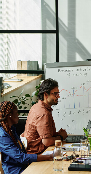 Two SEO specialists analyzing a performance graph on a whiteboard during a monthly strategy meeting. -  Rank Your Domain | SEO That Converts Clicks to Customers Two SEO specialists analyzing a performance graph on a whiteboard during a monthly strategy meeting.